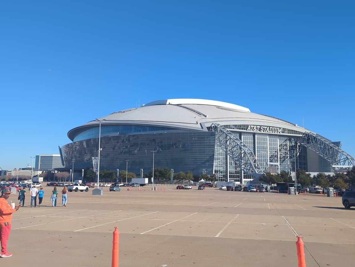 A large dome called AT&T Stadium with a retractrable roof with an empty parking lot in the foreground and 